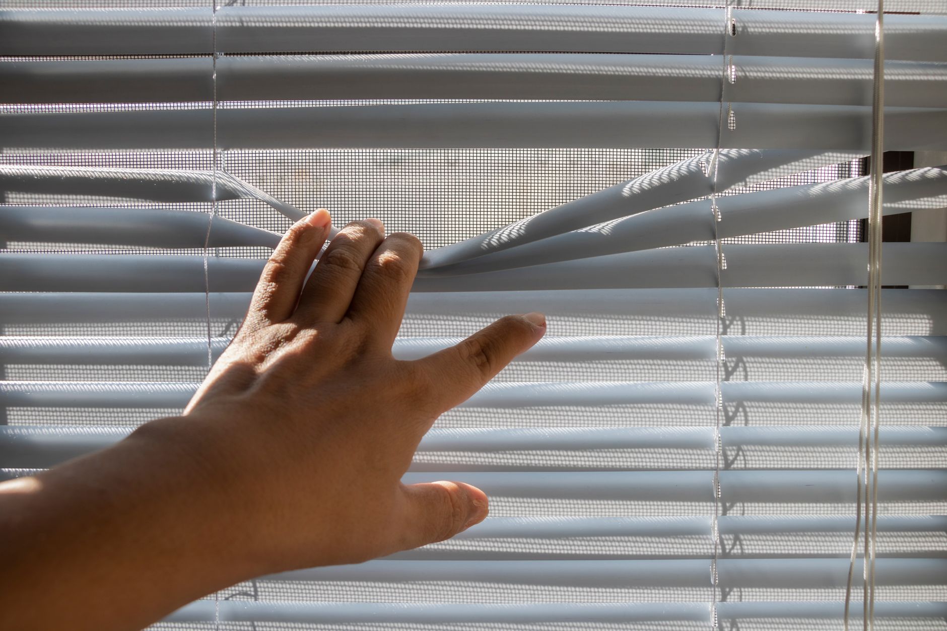 A hand checking bent slats on a window blind